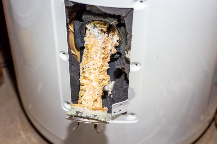 Repair and maintenance of boilers. A tubular electric heater covered with lime scale sticks out of the hole in the boiler.