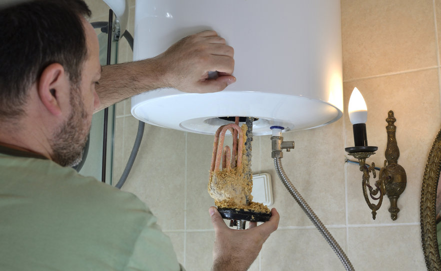 Man taking out an old water heater with scale deposition from a boiler in a bathroom