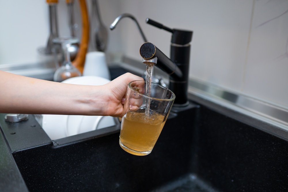 Close-up of a person holding a transparent cup under a stream of contaminated water