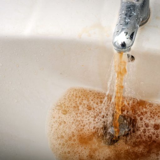 Grungy image of dirty brown water running from a water stained faucet