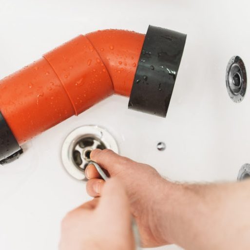 Plumber using drain snake to unclog bathtub.