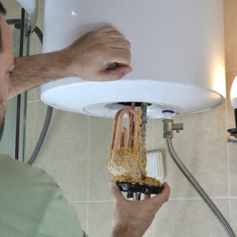 Man taking out an old water heater with scale deposition from a boiler in a bathroom