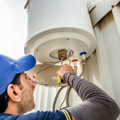 a professional electrician man is fixing a water heater at the roof top and wearing blue uniform and cap