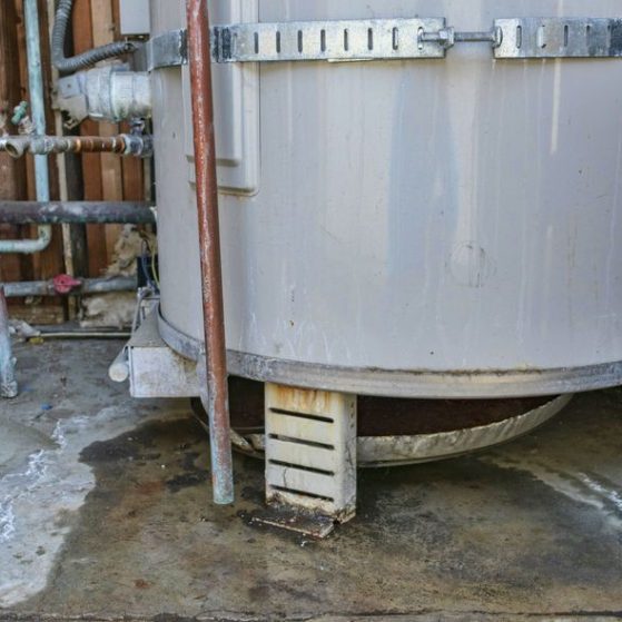 Water heater leaks from the bottom to the floor. Overflowing water heater drip pan. It is time to call a plumber service for inspection, repair or replacement.