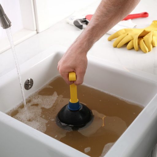 Man using plunger to unclog sink drain in kitchen, closeup